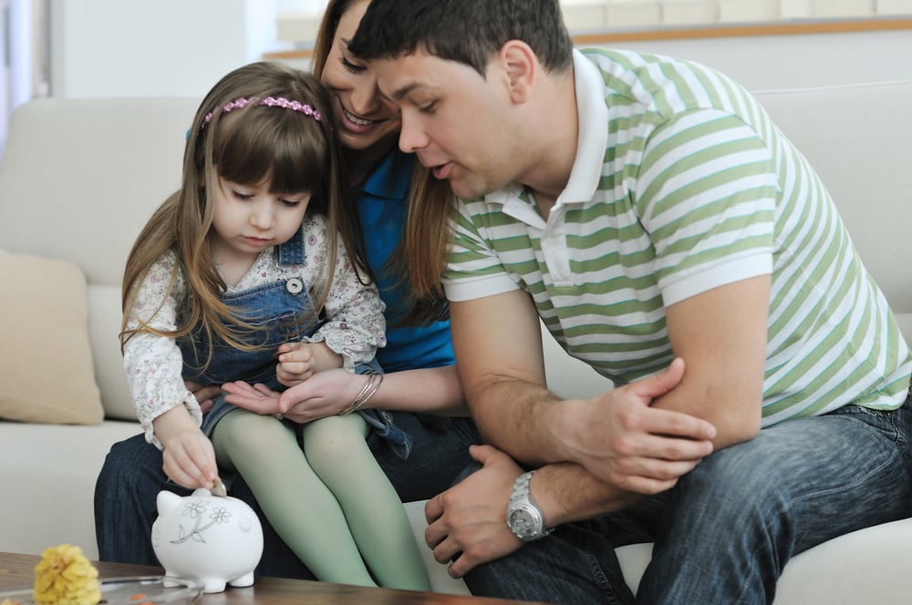 young parrent at home with beautiful child make savings and put coins money in piggy bank